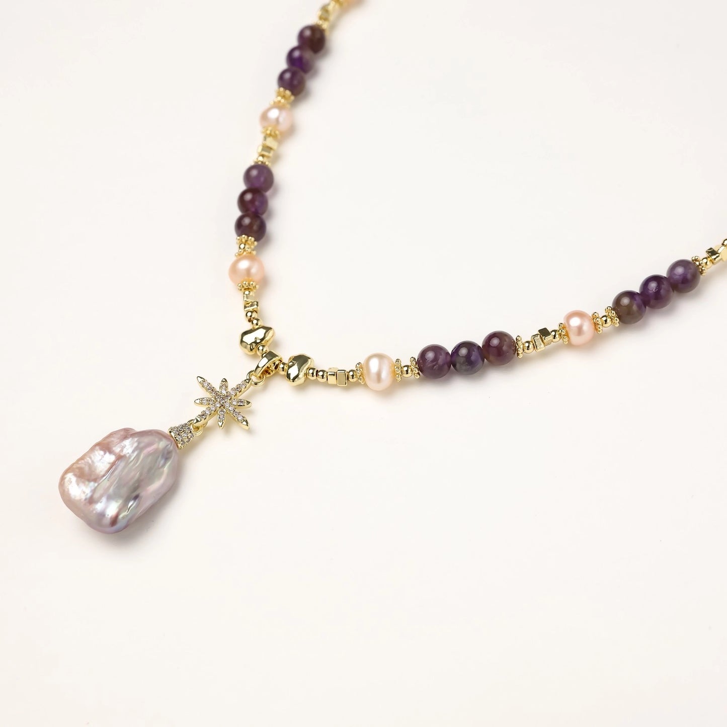 Gold-plated necklace with purple amethyst beads, pink pearls, and iridescent baroque pearl pendant beneath crystal star charm